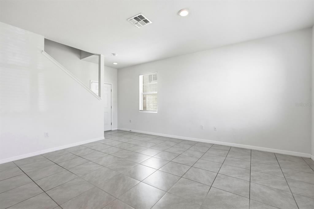 An empty room with light gray tile flooring, white walls, a window, and a staircase — 1680 COULTER LANE, PORT ORANGE, FL