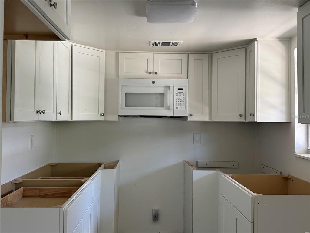 A kitchen with white cabinets, an over-the-range microwave, and unfinished base cabinets — 4609 MARINE PARKWAY UNIT 102, NEW PORT RICHEY, FL