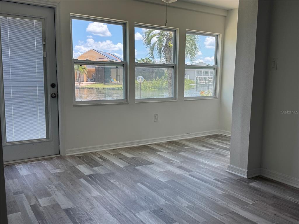 An empty room with wood-look flooring, three windows overlooking a canal, and a glass door — 4609 MARINE PARKWAY UNIT 102, NEW PORT RICHEY, FL