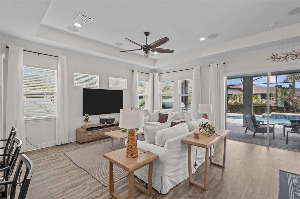 A living room features white sofas, a television, wood-look flooring, and sliding doors to a pool — 3164 SATILLA LOOP, ODESSA, FL