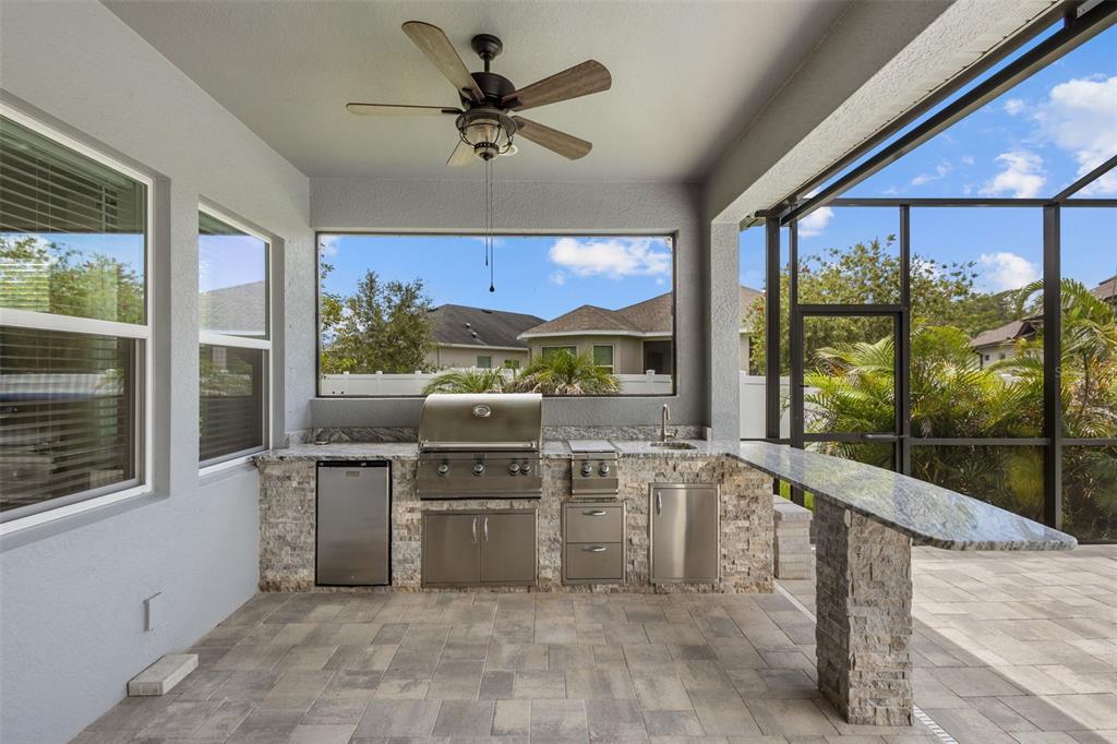 An outdoor kitchen with a grill, sink, and stone base sits on a covered patio — 3164 SATILLA LOOP, ODESSA, FL