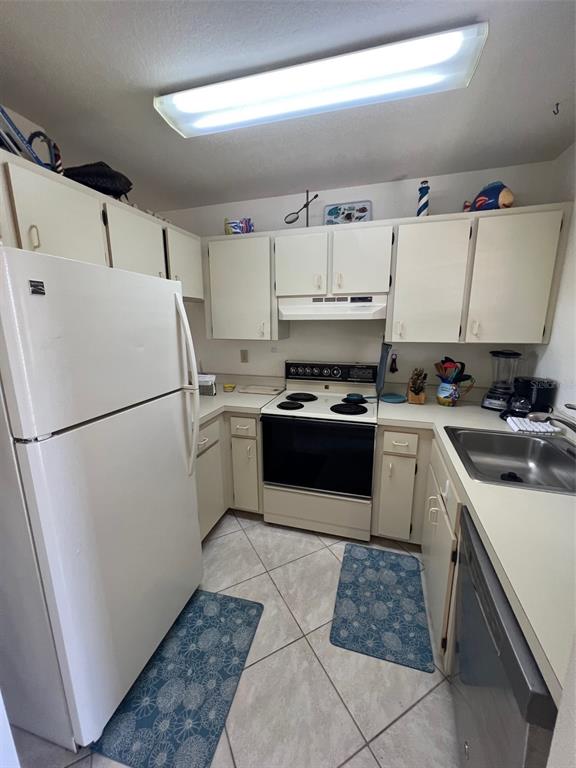 A small kitchen features white cabinets, a white refrigerator, a stove, and tiled flooring — 3221 WHITE IBIS COURT UNIT D3, PUNTA GORDA, FL