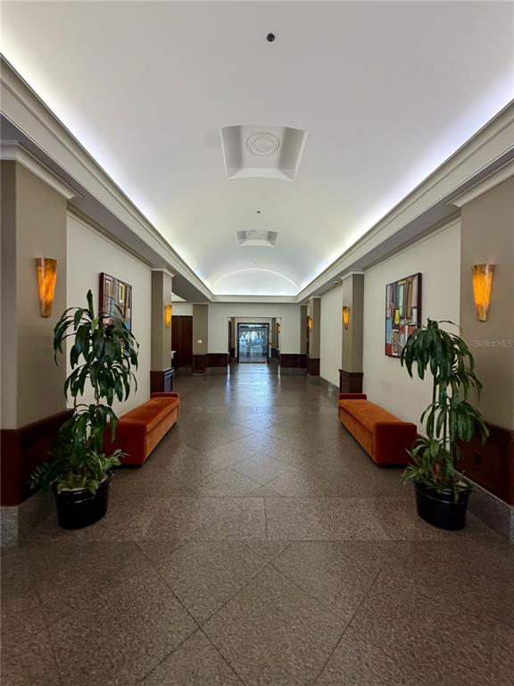 A symmetrical hallway features two potted plants, orange benches, wall sconces, and a vaulted ceiling — 50 CENTRAL AVENUE UNIT 970, SARASOTA, FL