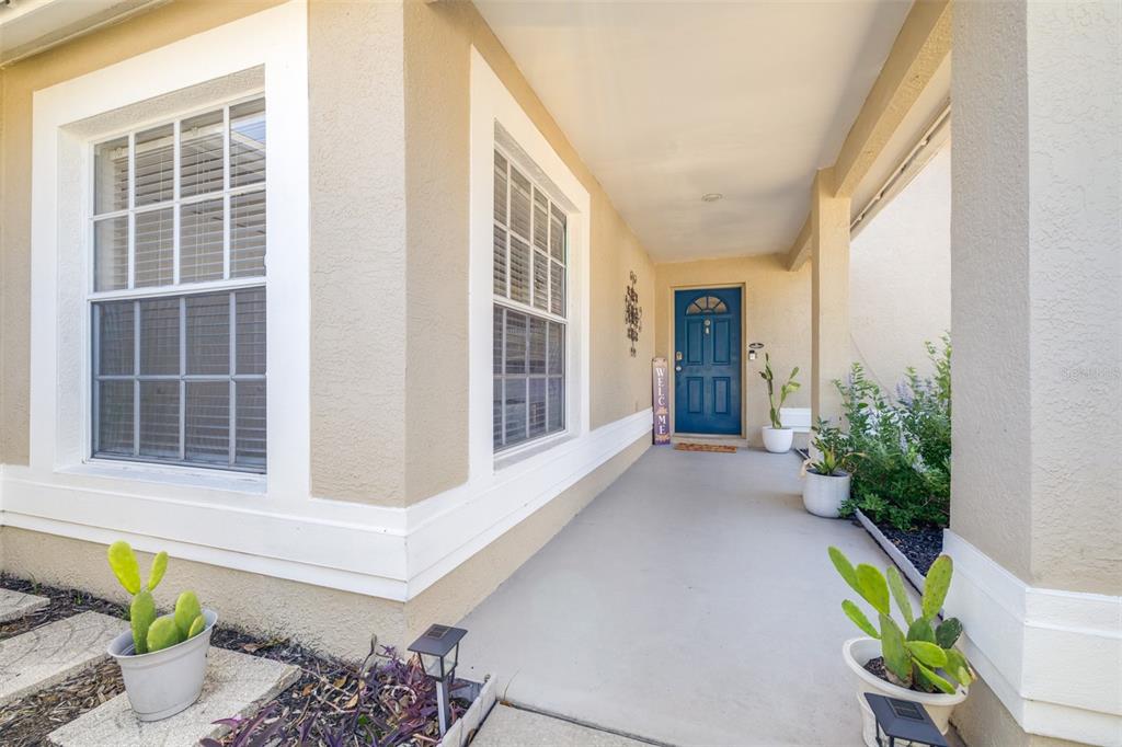 A covered front porch features a blue door, beige stucco walls, and potted cactus plants — 1016 MALLETWOOD DRIVE, BRANDON, FL