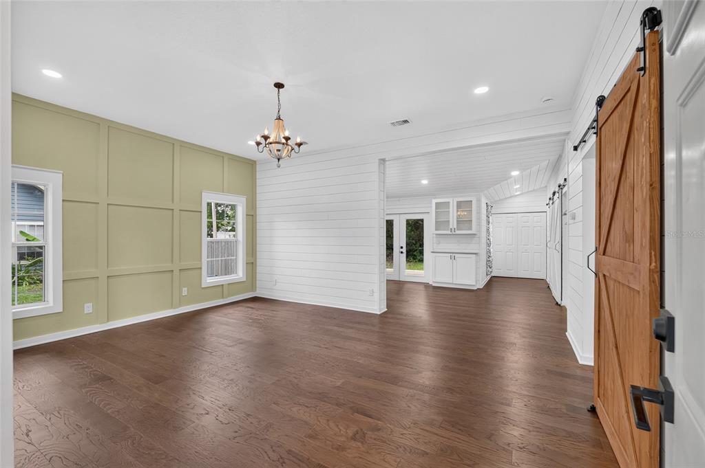 A room with wood floors, a green paneled wall, shiplap, and a sliding barn door — 220 NE 1ST AVENUE, WILLISTON, FL