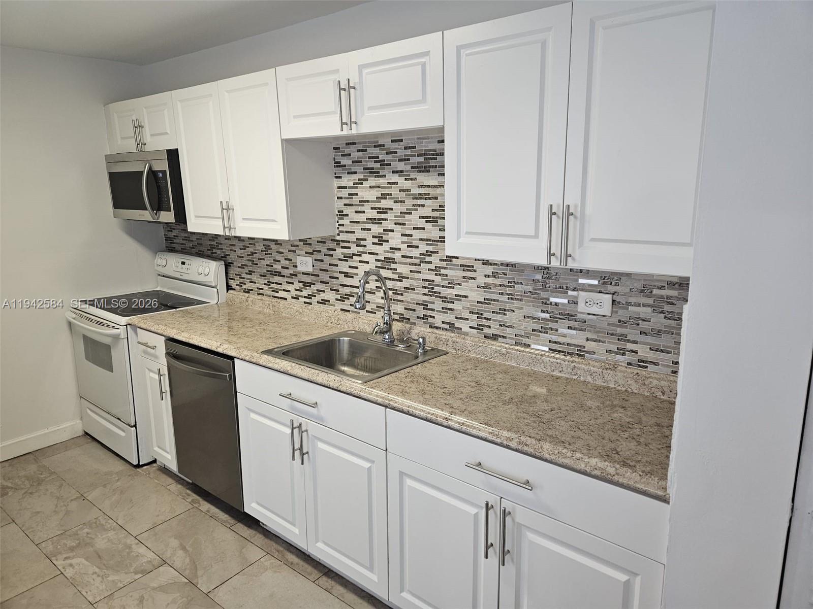 A kitchen features white cabinets, granite countertops, a stainless steel sink, and a tiled backsplash — 7135 Collins Ave # 1011, Miami Beach FL 33141, MIAMI BEACH, FL