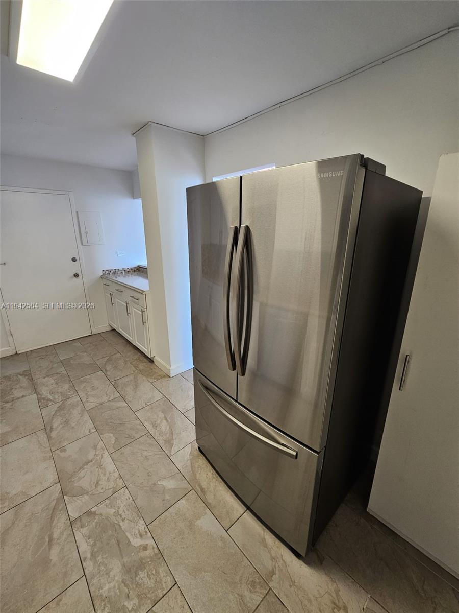 A stainless steel refrigerator stands in a kitchen with tiled floors and white cabinets — 7135 Collins Ave # 1011, Miami Beach FL 33141, MIAMI BEACH, FL
