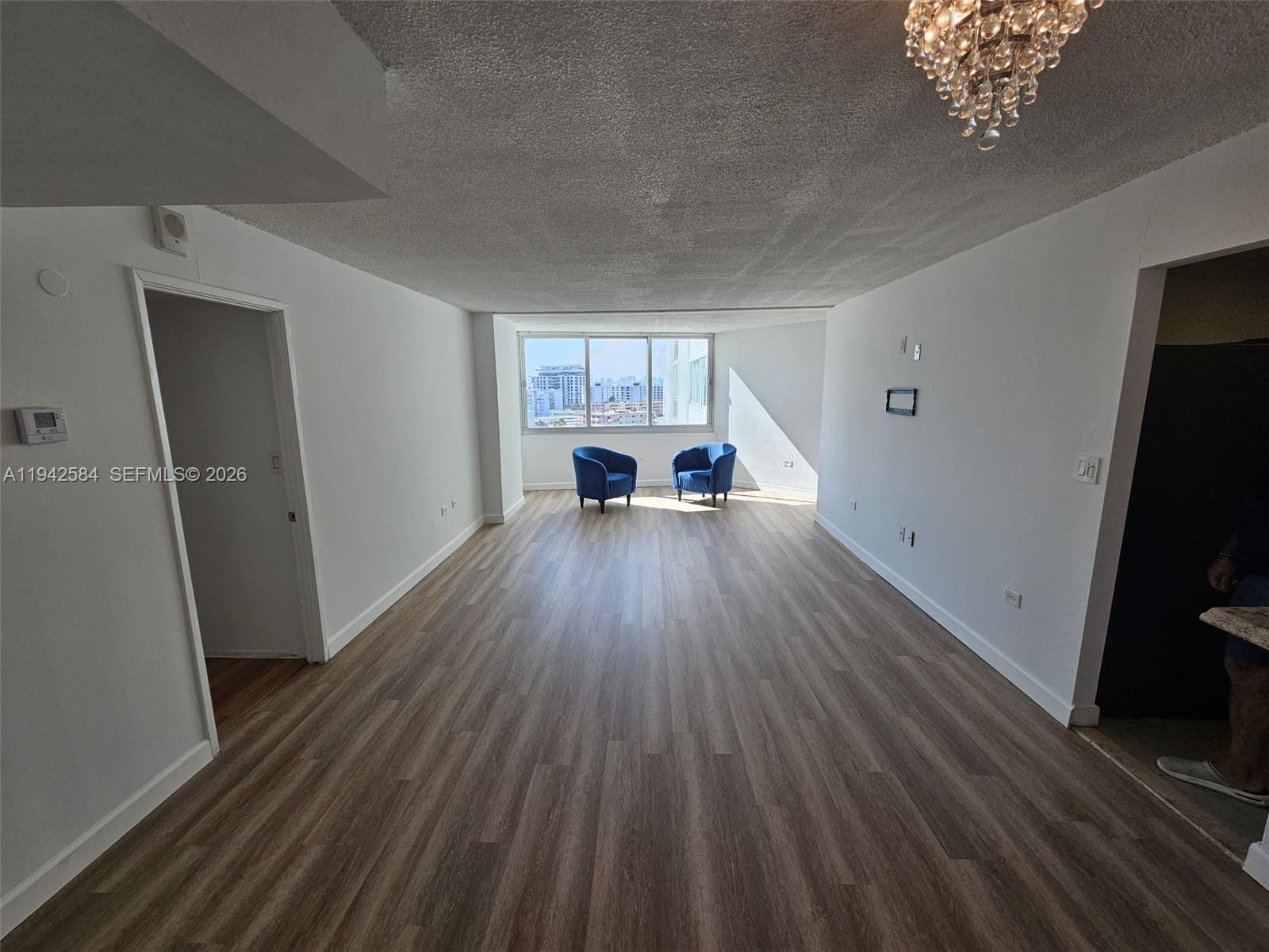 An empty living room features wood-look flooring, white walls, and two blue accent chairs — 7135 Collins Ave # 1011, Miami Beach FL 33141, MIAMI BEACH, FL
