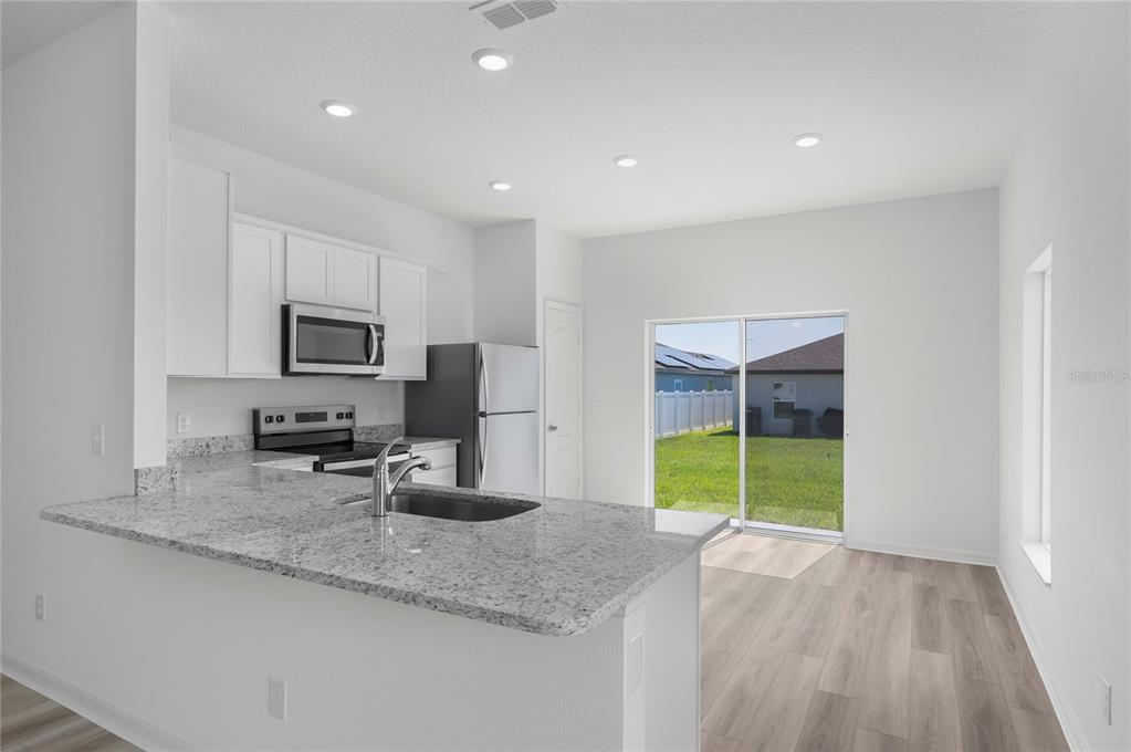 A kitchen with white cabinets, granite countertops, stainless steel appliances, and a sliding glass door — 3621 AMANATSU AVENUE, LAKE ALFRED, FL