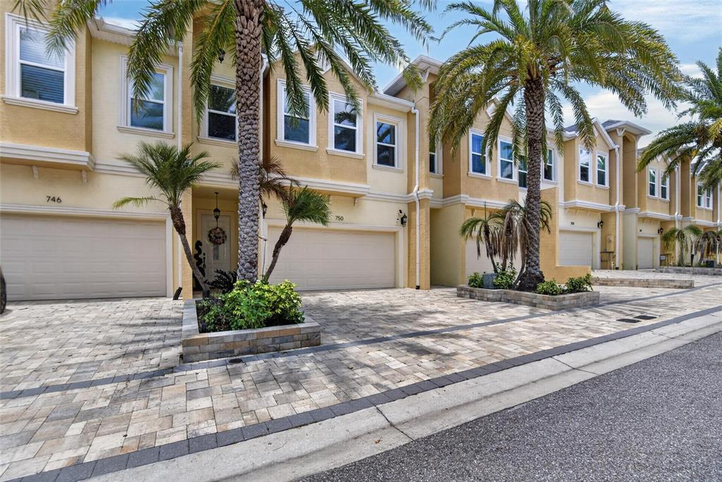 A row of multi-story townhomes with beige stucco facades, paver driveways, and palm trees — 750 GRAND CYPRESS LANE, TARPON SPRINGS, FL