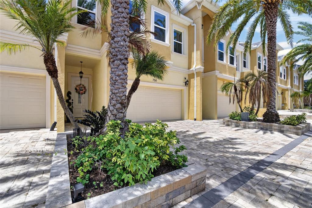 A multi-story townhouse exterior features a paved driveway, palm trees, and a small garden bed — 750 GRAND CYPRESS LANE, TARPON SPRINGS, FL