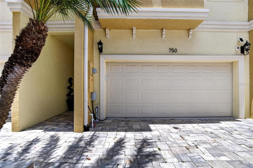 A beige garage door with the number 750 above it sits beside a palm tree — 750 GRAND CYPRESS LANE, TARPON SPRINGS, FL