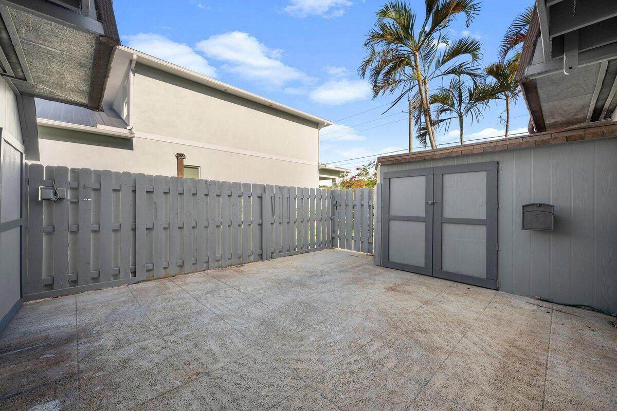 A concrete patio features a gray wooden fence, a storage shed, and palm trees above — 1980 NE Dixie Highway, Jensen Beach FL 34957, JENSEN BEACH, FL