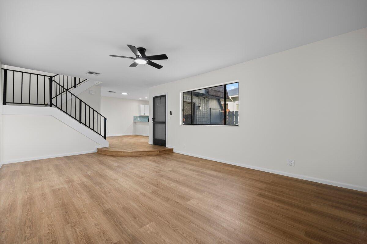 A living room features wood-look flooring, a staircase with black railings, and a ceiling fan — 1980 NE Dixie Highway, Jensen Beach FL 34957, JENSEN BEACH, FL