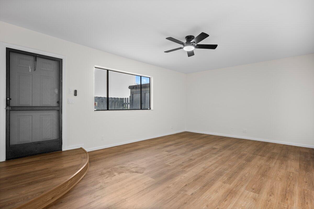 An empty room features light wood-look flooring, white walls, a ceiling fan, and a door — 1980 NE Dixie Highway, Jensen Beach FL 34957, JENSEN BEACH, FL