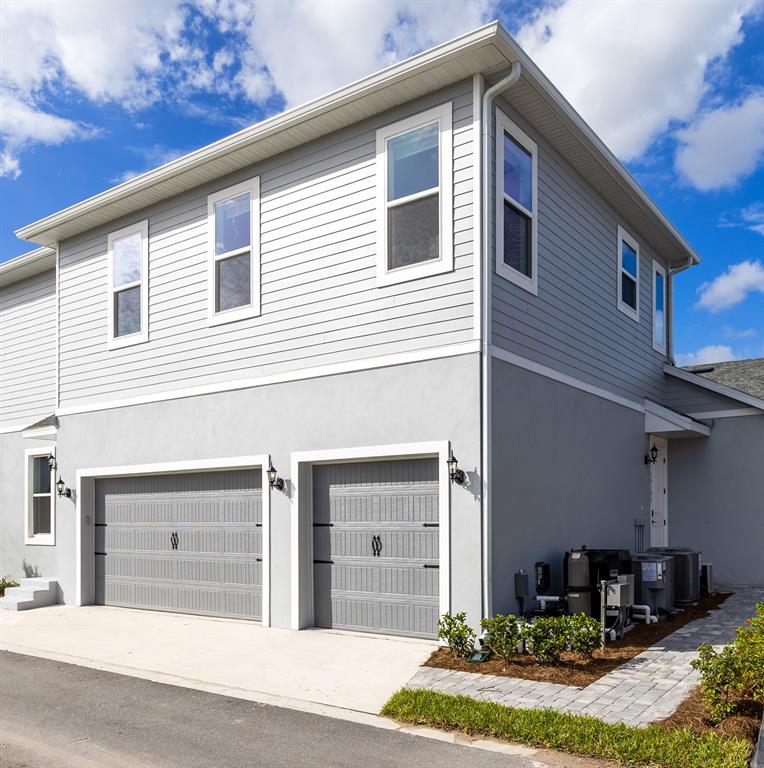 A two-story house exterior features gray horizontal siding, stucco lower walls, and two garage doors — 10105 HASSELMANN ALLEY, ORLANDO, FL