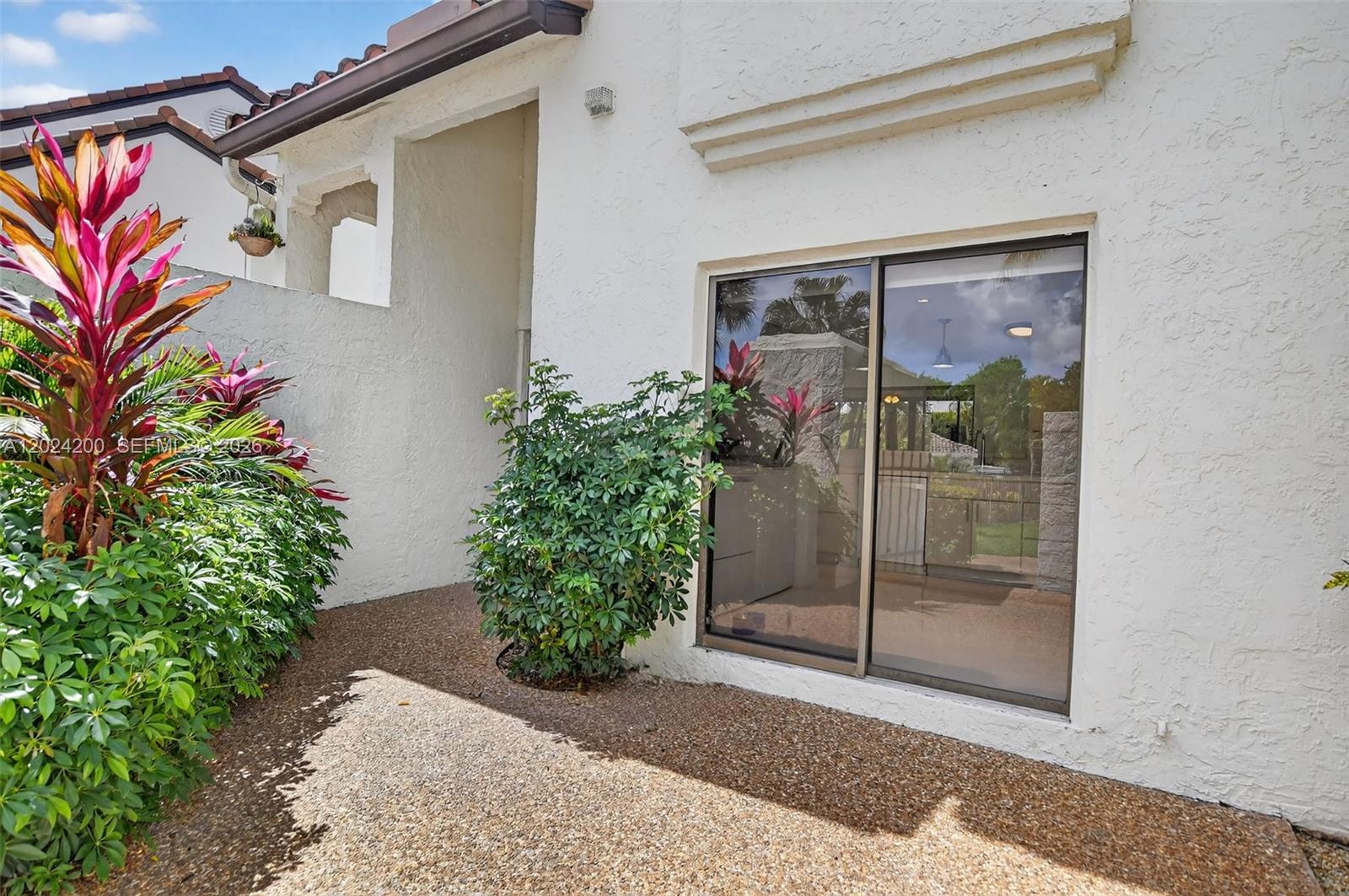 A white stucco exterior wall features a sliding glass door next to a green shrub — 7906 Granada Pl # 1201, Boca Raton FL 33433, BOCA RATON, FL