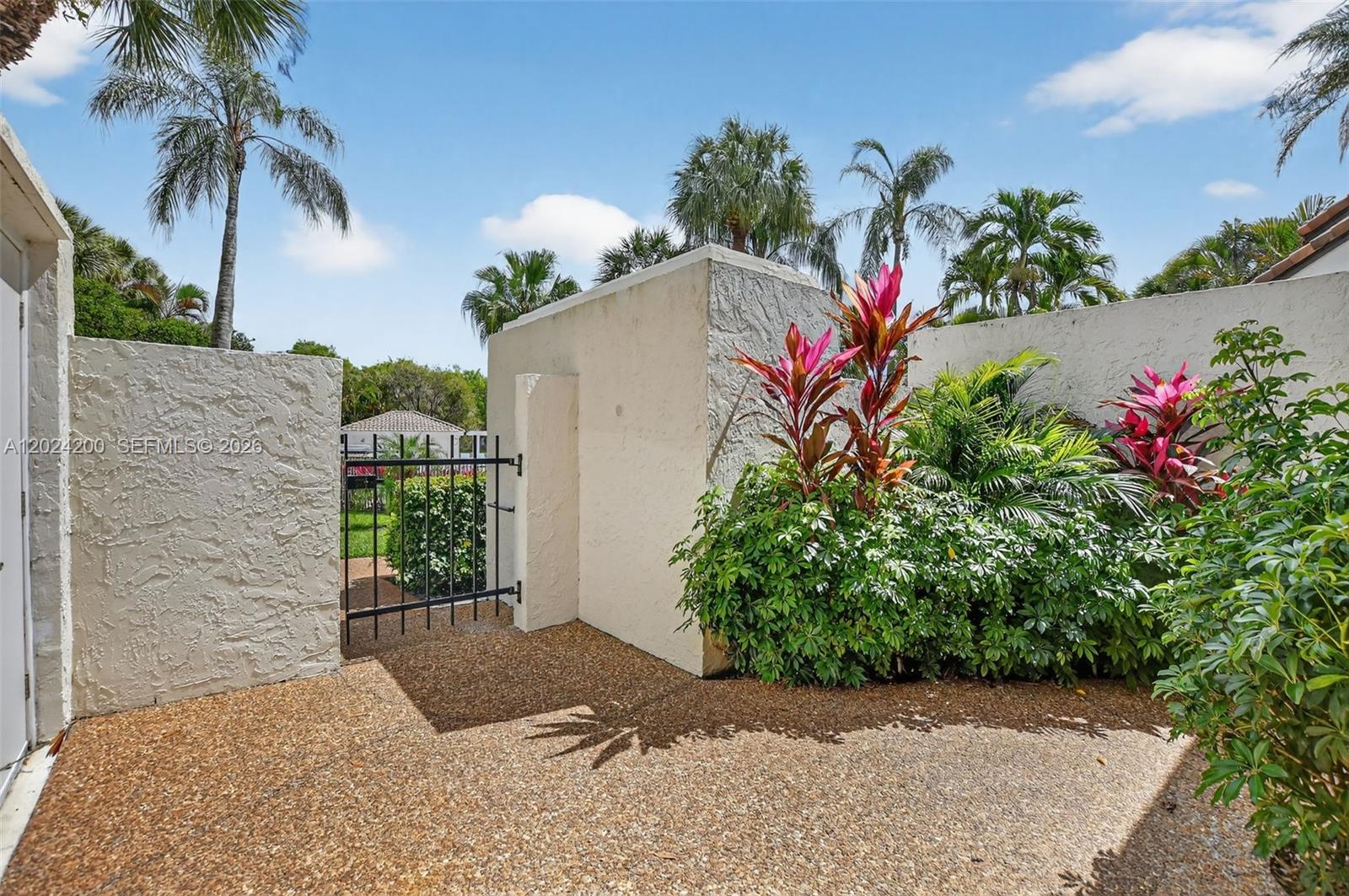 A gravel patio features a black metal gate set between textured stucco walls and landscaping — 7906 Granada Pl # 1201, Boca Raton FL 33433, BOCA RATON, FL