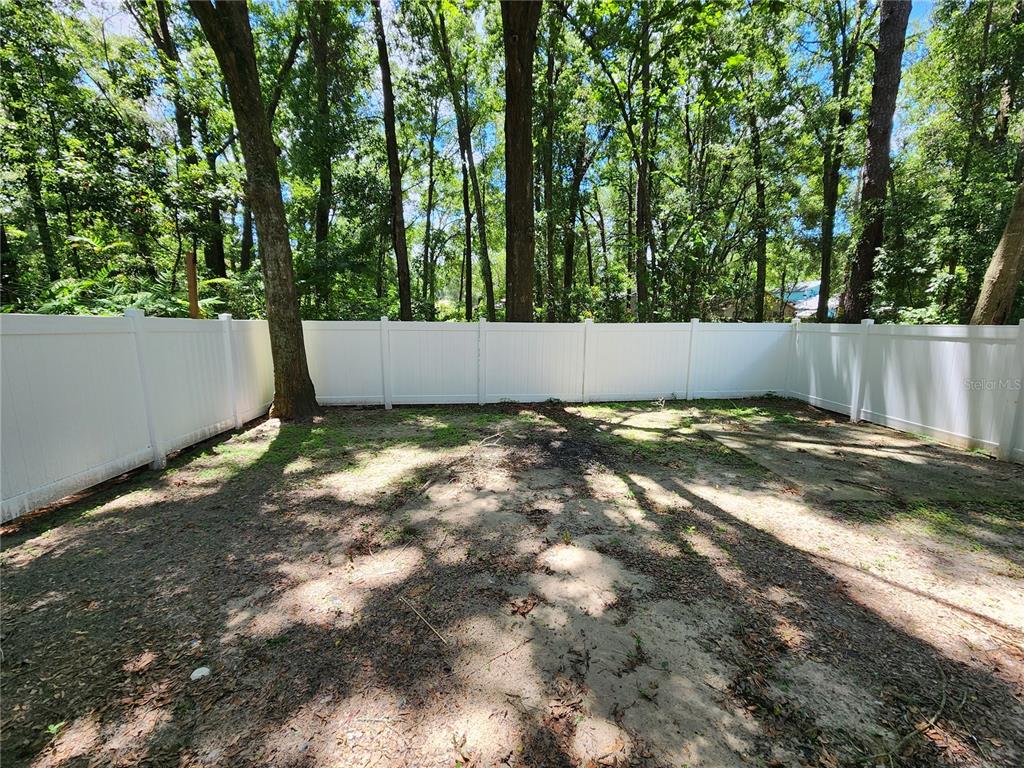 A fenced backyard with sandy ground, scattered leaves, and tall trees in the background — 2018 SW 70TH TERRACE, GAINESVILLE, FL