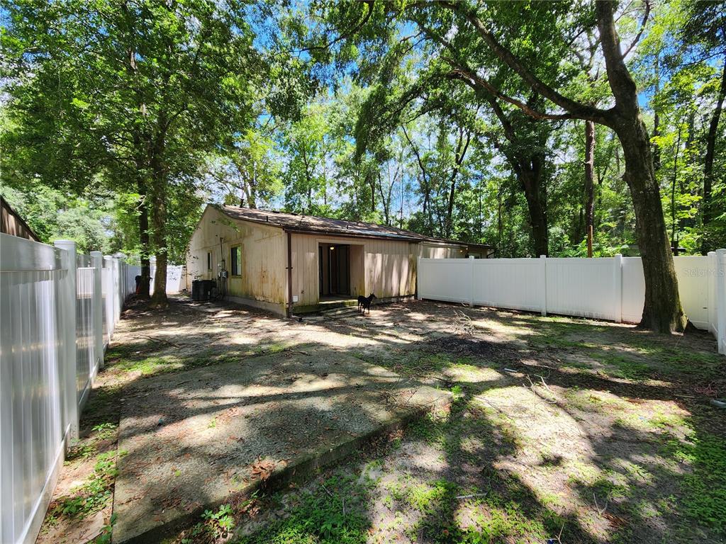 The backyard of a house features a concrete patio, a white vinyl fence, and trees — 2018 SW 70TH TERRACE, GAINESVILLE, FL