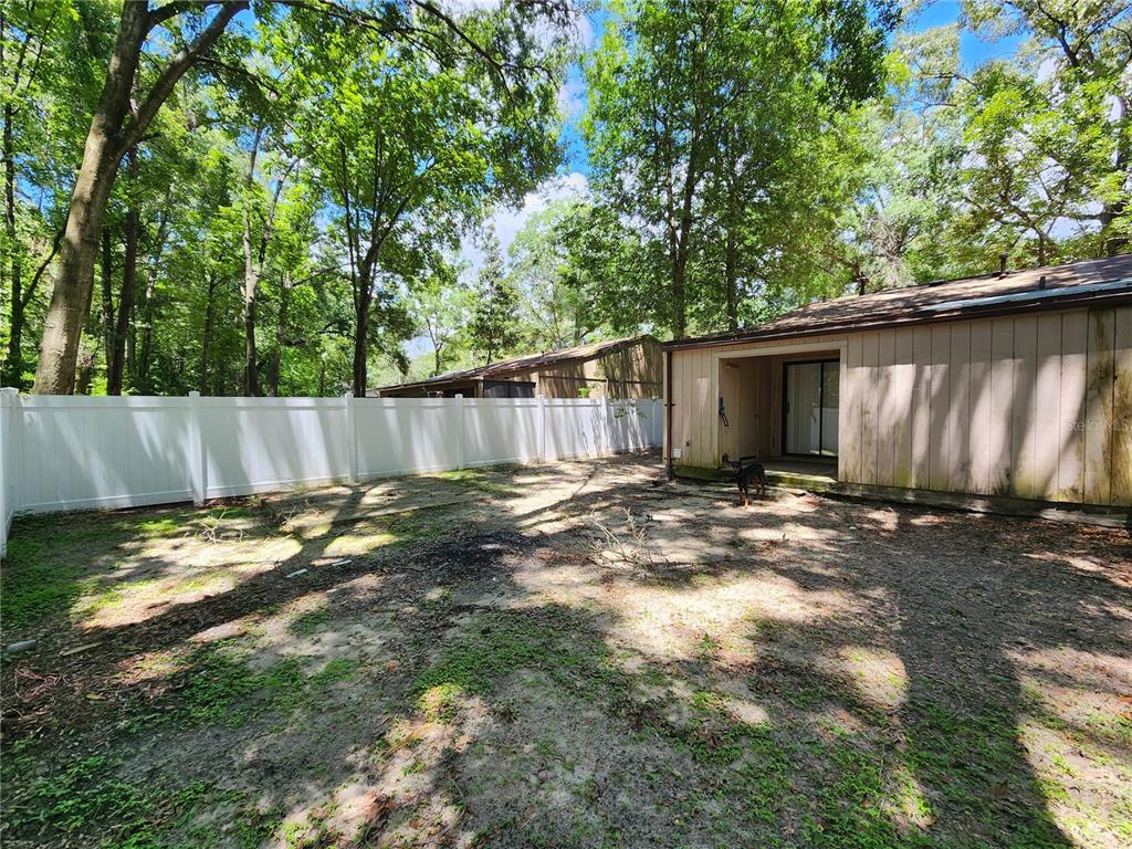 A backyard with a white vinyl fence, a concrete patio, and mature trees — 2018 SW 70TH TERRACE, GAINESVILLE, FL