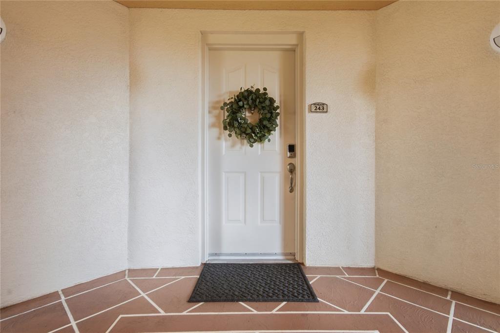 A white front door with a wreath and house number 243 sits on a tiled porch — 12055 GANDY BOULEVARD N UNIT 243, ST PETERSBURG, FL