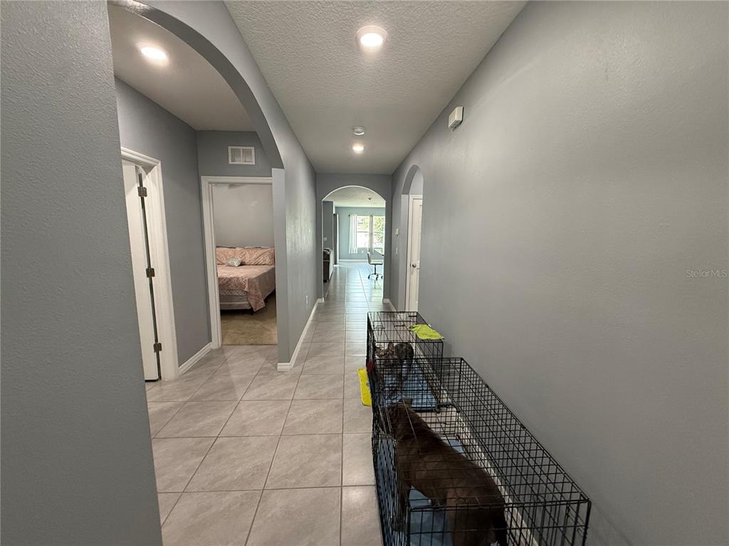 A tiled hallway features arched doorways, gray walls, and two dog crates containing dogs — 635 AUTUMN STREAM DRIVE, AUBURNDALE, FL