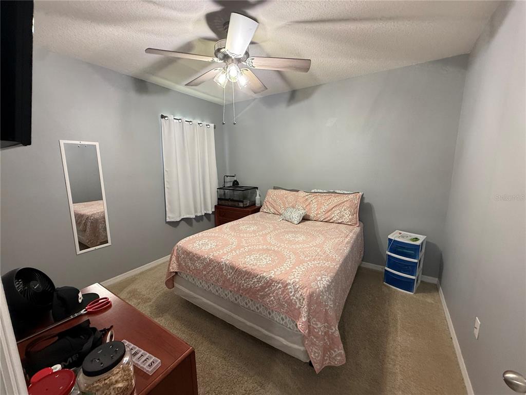 A bedroom with gray walls, a ceiling fan, a bed with pink bedding, and carpeted flooring — 635 AUTUMN STREAM DRIVE, AUBURNDALE, FL