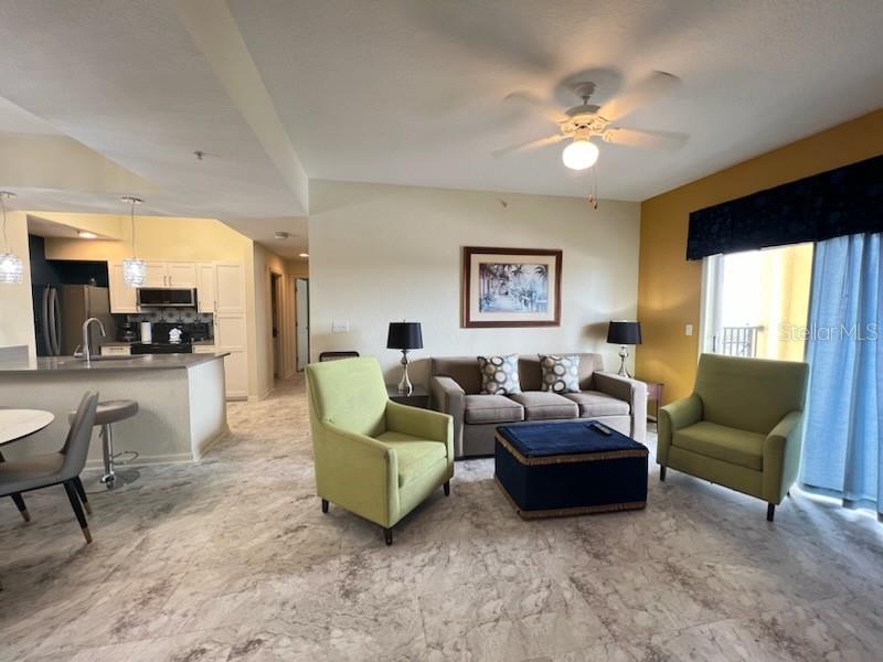 A living room with light tile floors, two green armchairs, a sofa, and an open kitchen — 8000 POINCIANA BOULEVARD UNIT 2705, ORLANDO, FL