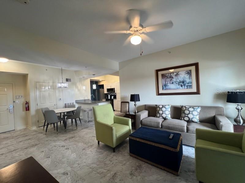 A living room with light tile floors, a sofa, two green armchairs, and a kitchen — 8000 POINCIANA BOULEVARD UNIT 2705, ORLANDO, FL