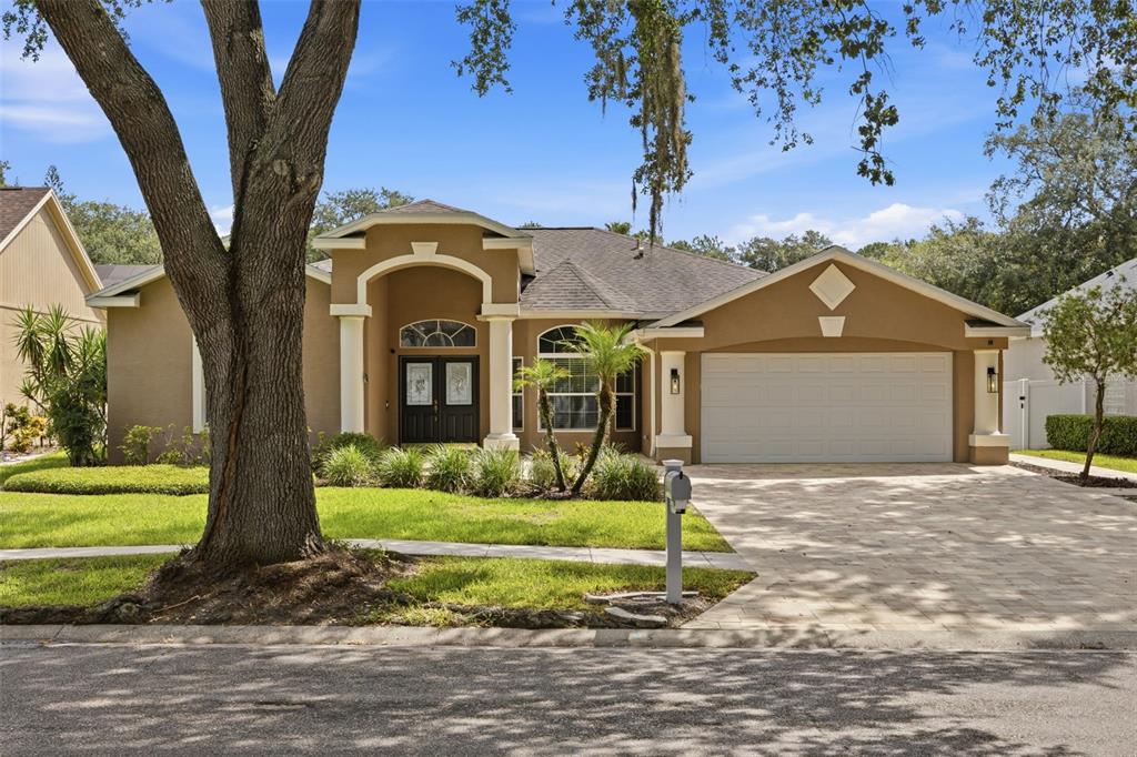 A single-story tan house with a paved driveway, arched entryway, and a large front tree — 7208 YARDLEY WAY, TAMPA, FL
