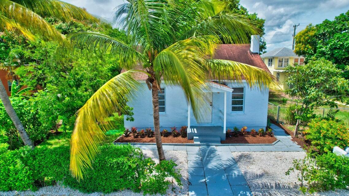 A small, light blue cottage with a red roof stands behind a palm tree — 415 N H Street, FL 33460, FL