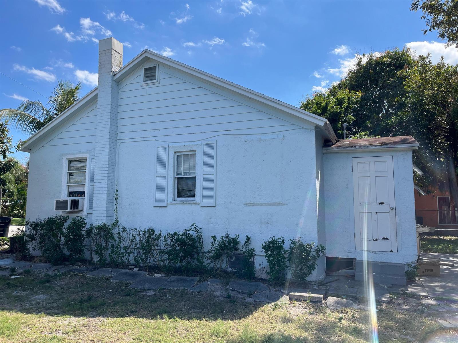 A light blue, single-story house exterior features a brick chimney, white shutters, and a side door — 415 N H Street, FL 33460, FL