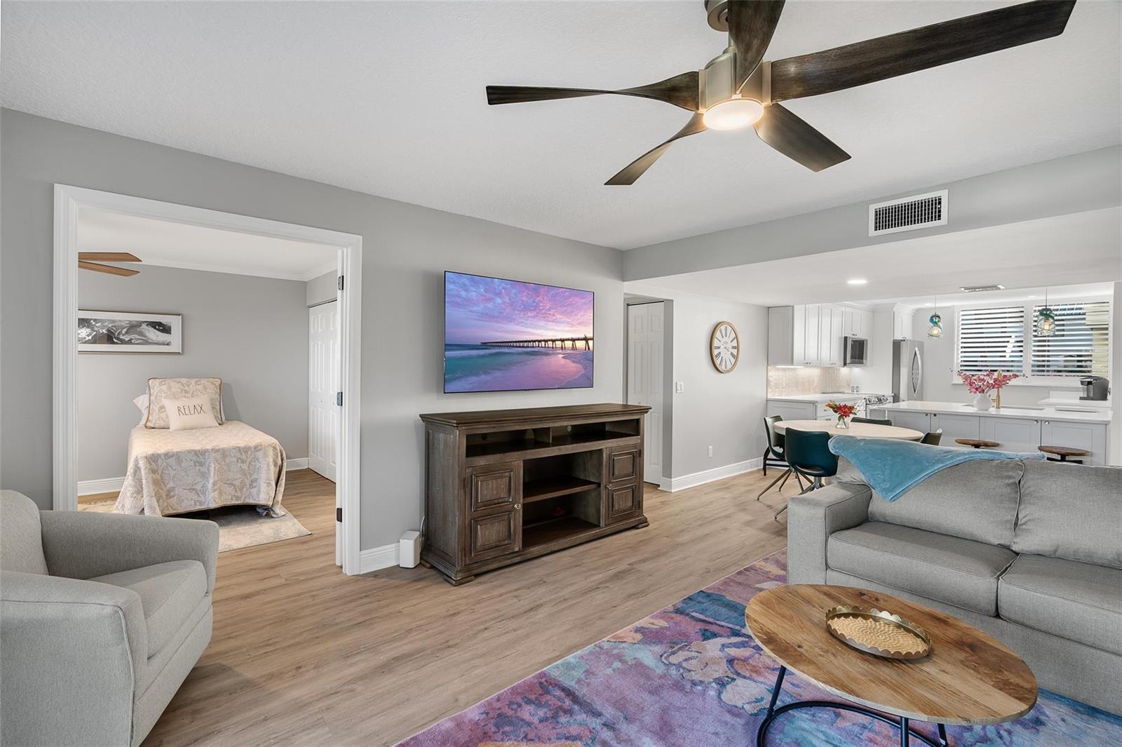 A living room with a television, wooden media console, and an adjacent bedroom and kitchen — 1825 Tarpon Lane # 106, Vero Beach FL 32960, VERO BEACH, FL