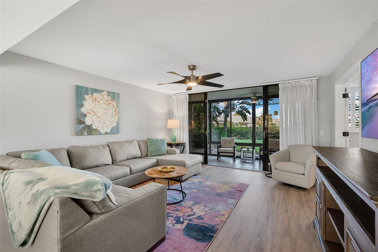A living room features a gray sectional sofa, a colorful rug, and sliding glass patio doors — 1825 Tarpon Lane # 106, Vero Beach FL 32960, VERO BEACH, FL