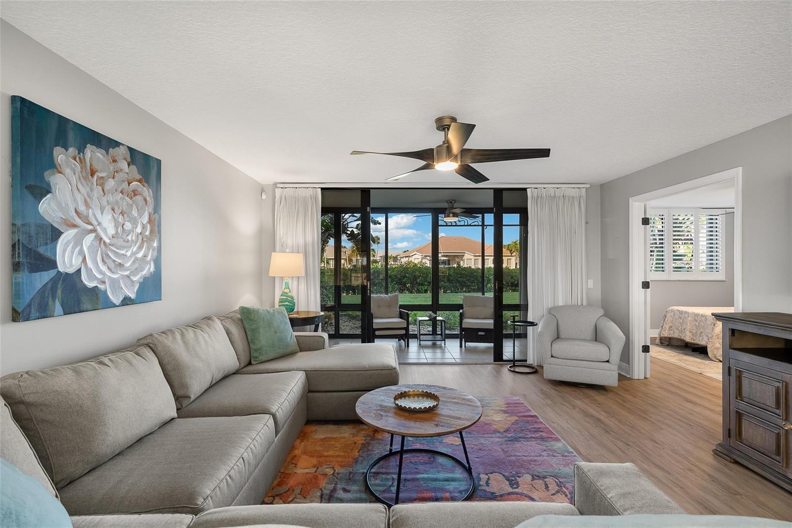 A living room features a sectional sofa, a colorful rug, and sliding doors to a lanai — 1825 Tarpon Lane # 106, Vero Beach FL 32960, VERO BEACH, FL
