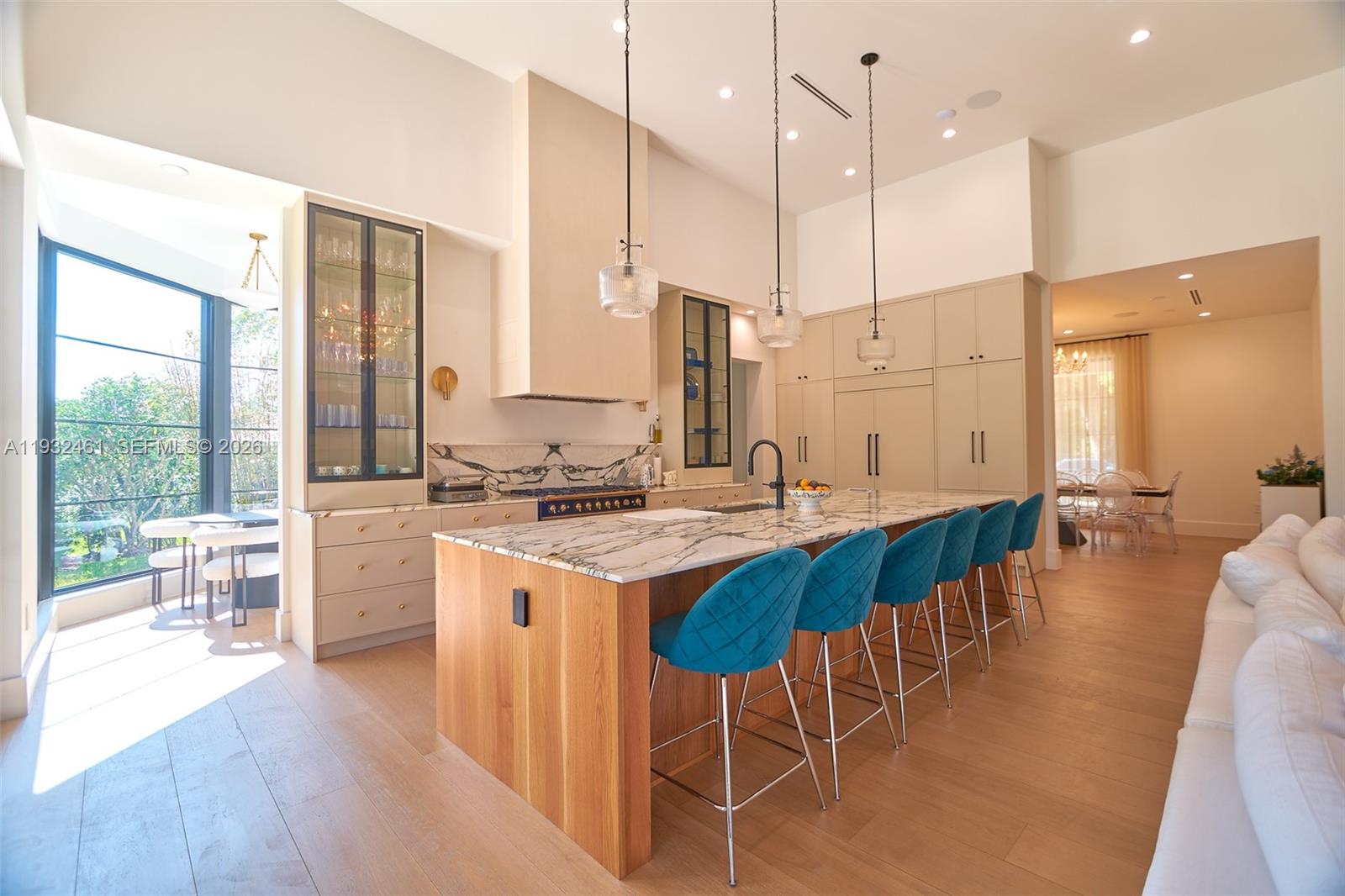 A modern kitchen features a marble island with blue velvet stools and light wood cabinetry — 11001 SW 74th Ave, Pinecrest FL 33156, PINECREST, FL