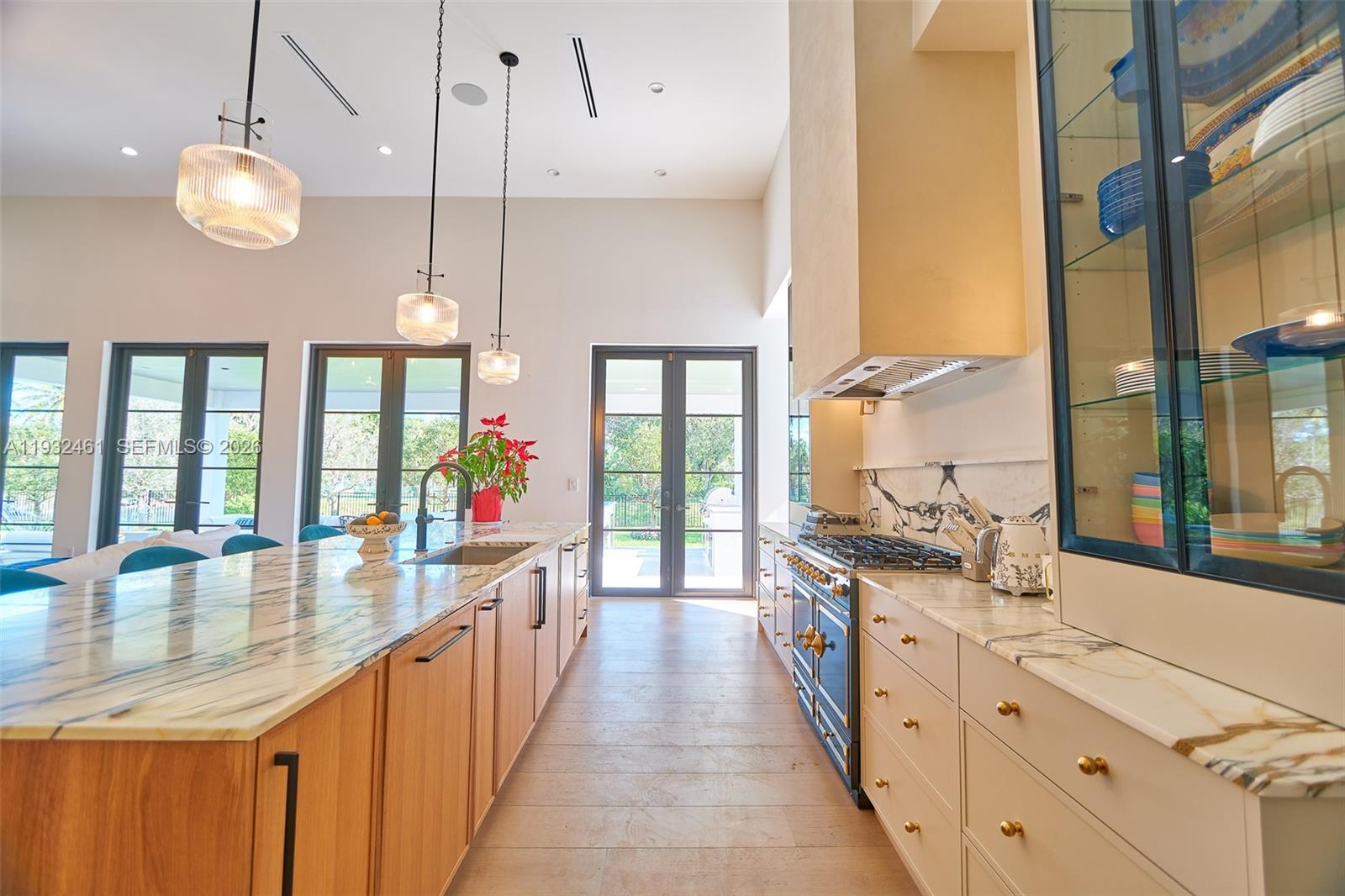 A modern kitchen features a marble-topped island, light wood cabinetry, and a dark range — 11001 SW 74th Ave, Pinecrest FL 33156, PINECREST, FL
