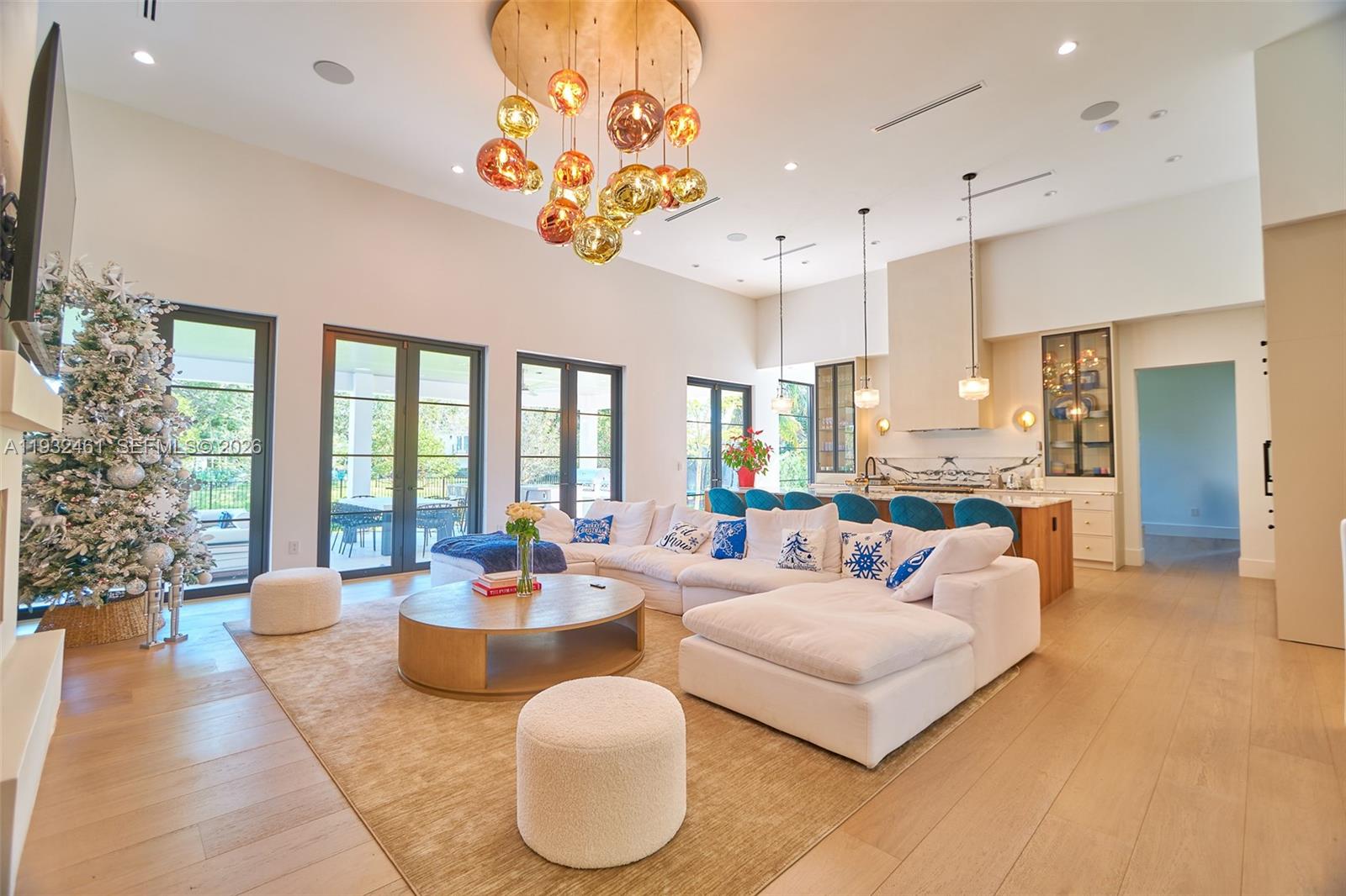 A spacious open-concept living room features a large white sectional, a modern chandelier, and flooring — 11001 SW 74th Ave, Pinecrest FL 33156, PINECREST, FL