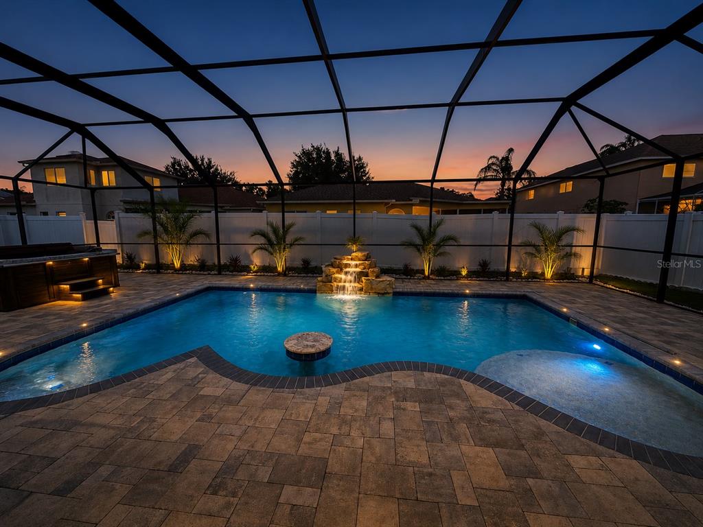 A screened-in backyard pool area features a stone waterfall, a spa, and paver decking — 15911 MUIRFIELD DRIVE, ODESSA, FL