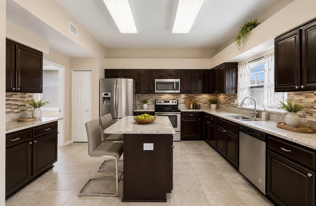 A kitchen with dark wood cabinets, granite countertops, a center island, and stainless steel appliances — 15911 MUIRFIELD DRIVE, ODESSA, FL