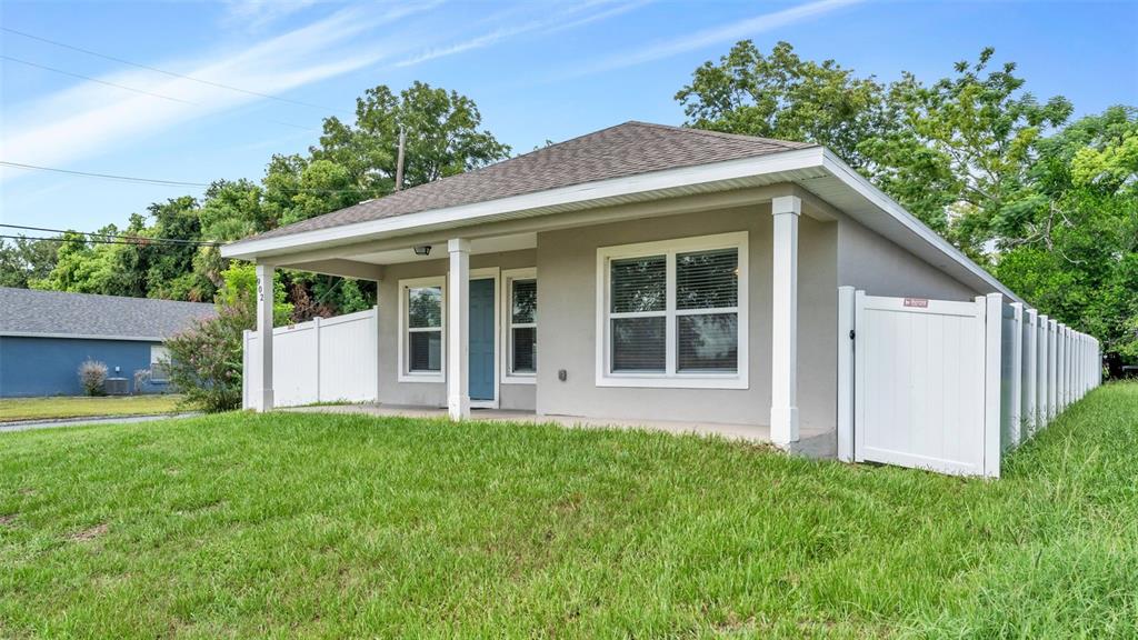 A single-story house with a covered front porch, gray stucco exterior, and white vinyl fencing — 902 N VERMONT AVENUE, LAKELAND, FL