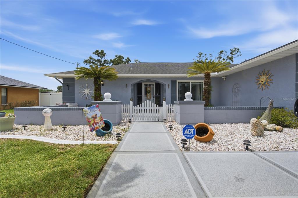 A single-story house features a gray exterior, a gated courtyard, and a paved walkway — 13220 LINDEN DRIVE, SPRING HILL, FL