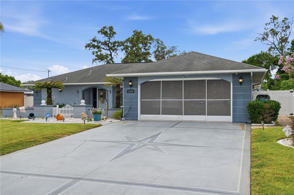A single-story house with a blue exterior, a screened garage, and a decorative concrete driveway — 13220 LINDEN DRIVE, SPRING HILL, FL