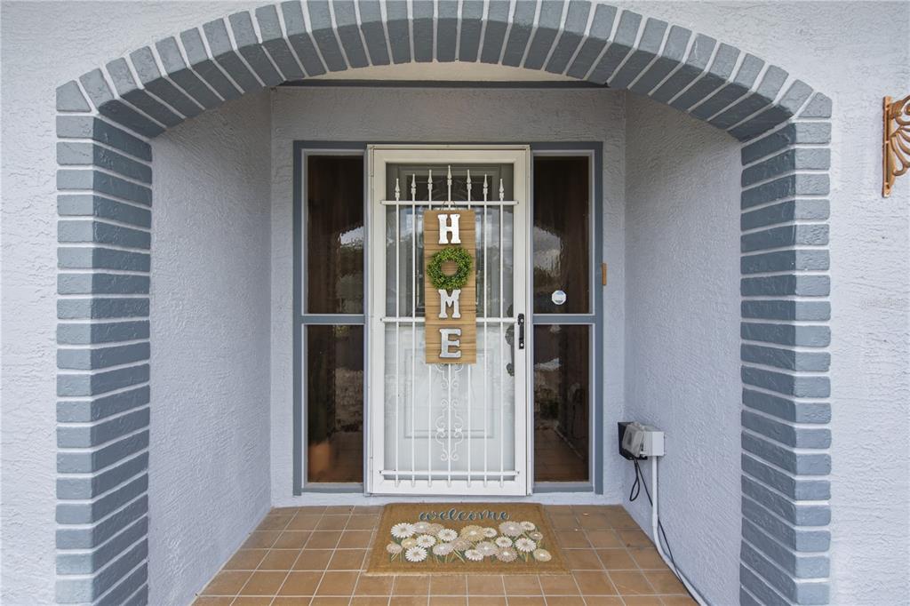 A front entryway features a white storm door with a decorative sign and tiled porch — 13220 LINDEN DRIVE, SPRING HILL, FL