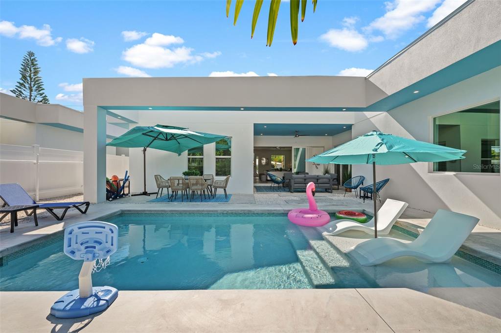 A backyard patio features a swimming pool with lounge chairs, umbrellas, and outdoor dining furniture — 2365 WALDEMERE STREET, SARASOTA, FL