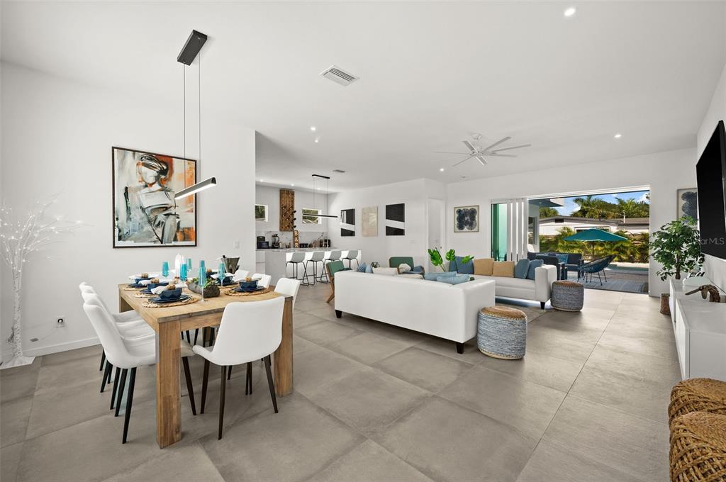 An open-concept living and dining area features large floor tiles, white furniture, and sliding glass doors — 2365 WALDEMERE STREET, SARASOTA, FL