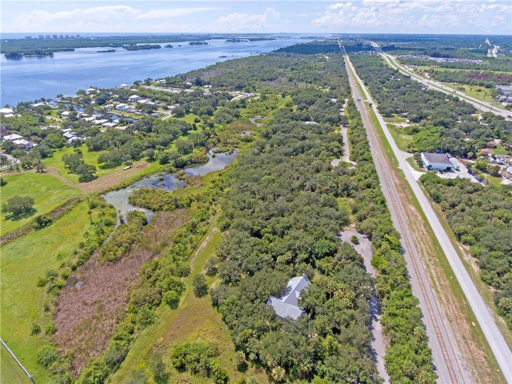 An aerial view shows a house nestled in trees next to a pond and railroad tracks — 4108 Mariner Oaks Way, FL 34946, FL