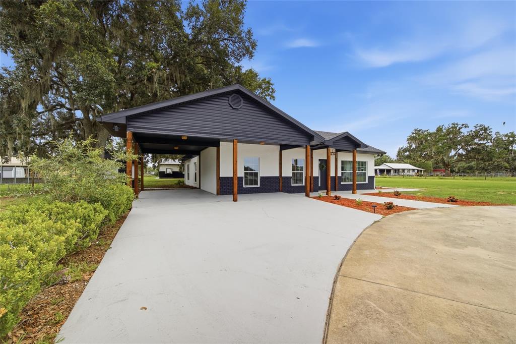 A single-story house with a dark-colored carport, white walls, and a concrete driveway — 1205 E KNIGHTS GRIFFIN ROAD, PLANT CITY, FL