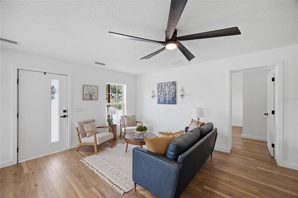 A living room features white walls, wood-look flooring, a ceiling fan, and a dark sofa — 1205 E KNIGHTS GRIFFIN ROAD, PLANT CITY, FL